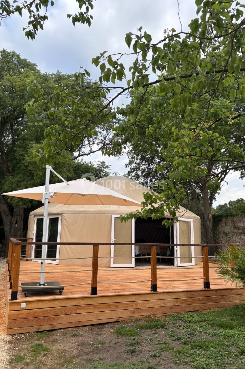 Tente de style yourte avec terrasse en bois, entourée d'arbres dans un cadre naturel.