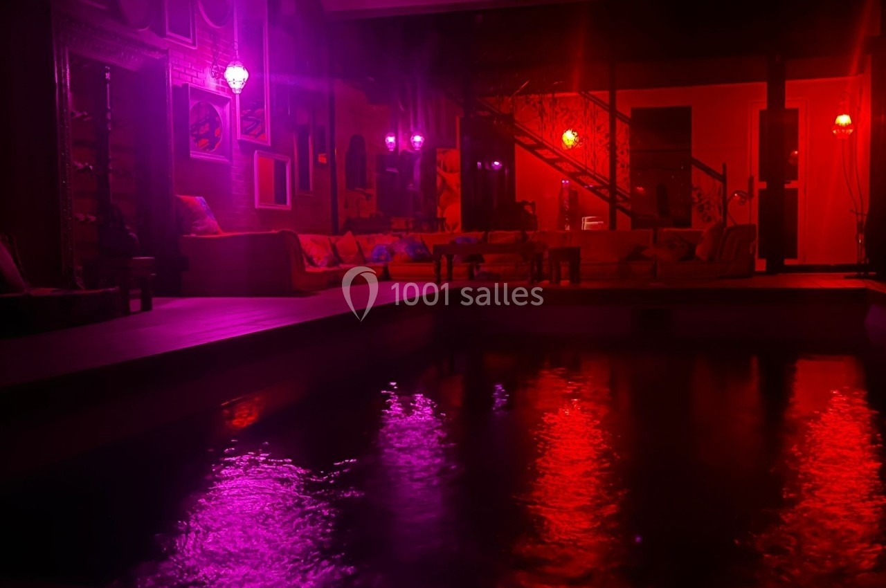 Espace intérieur avec piscine éclairée par des lumières rouges et violettes, ambiance tamisée et chaleureuse.
