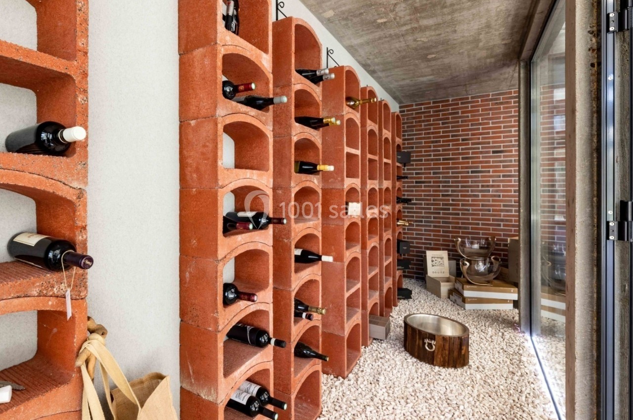 Cave à vin avec étagères en briques rouges, bouteilles rangées et sol recouvert de gravier blanc.