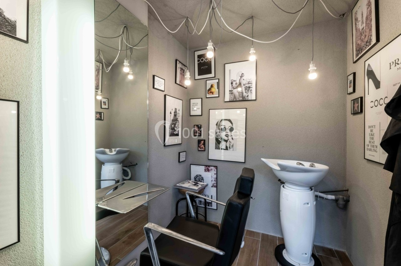 Coin de salon de coiffure avec un fauteuil, un lavabo, des miroirs et des cadres décoratifs accrochés au mur.
