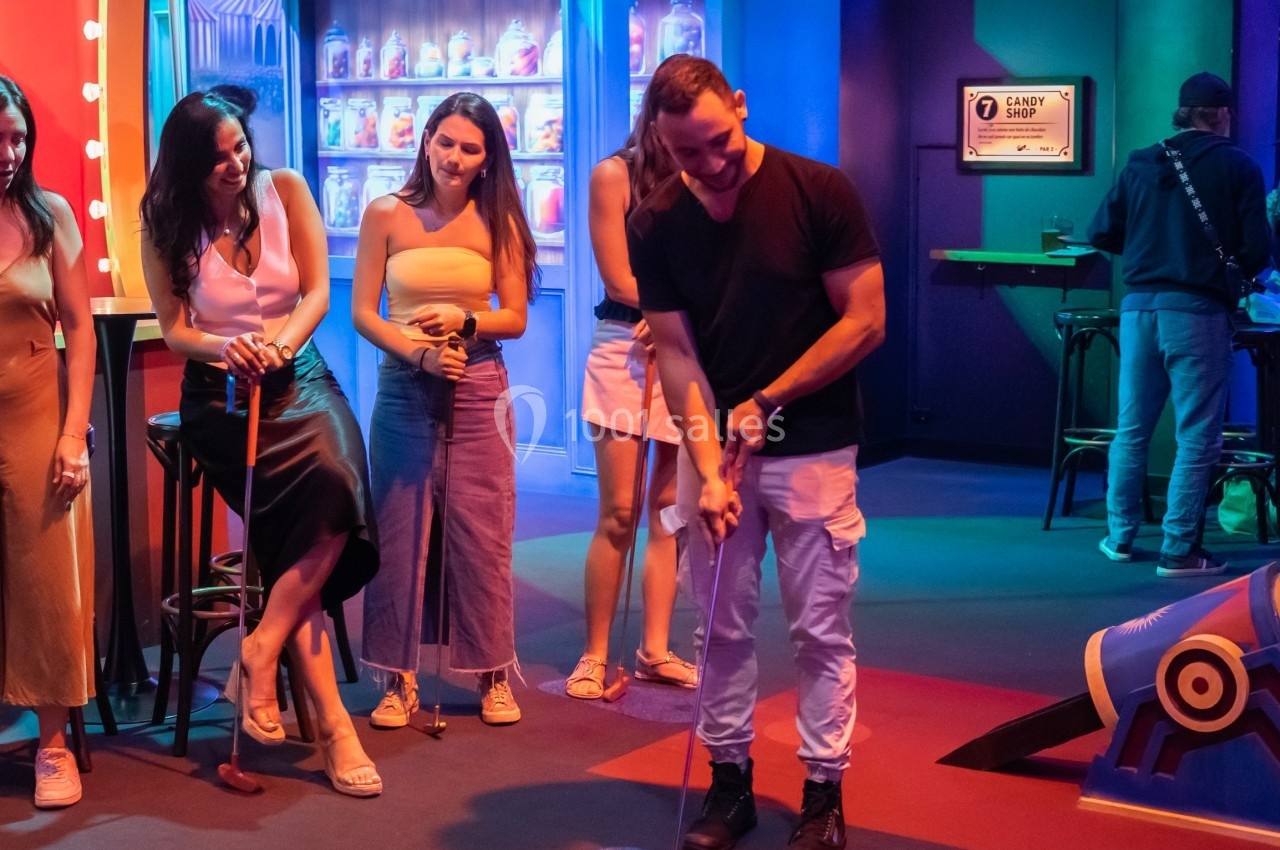 Un groupe de personnes observe un homme jouant à un jeu interactif dans un espace coloré et lumineux.
