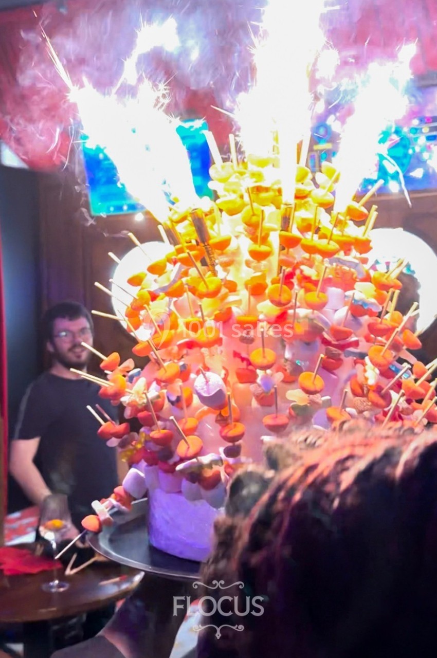 Gâteau festif décoré de brochettes de bonbons et de cierges magiques allumés dans une ambiance de fête.