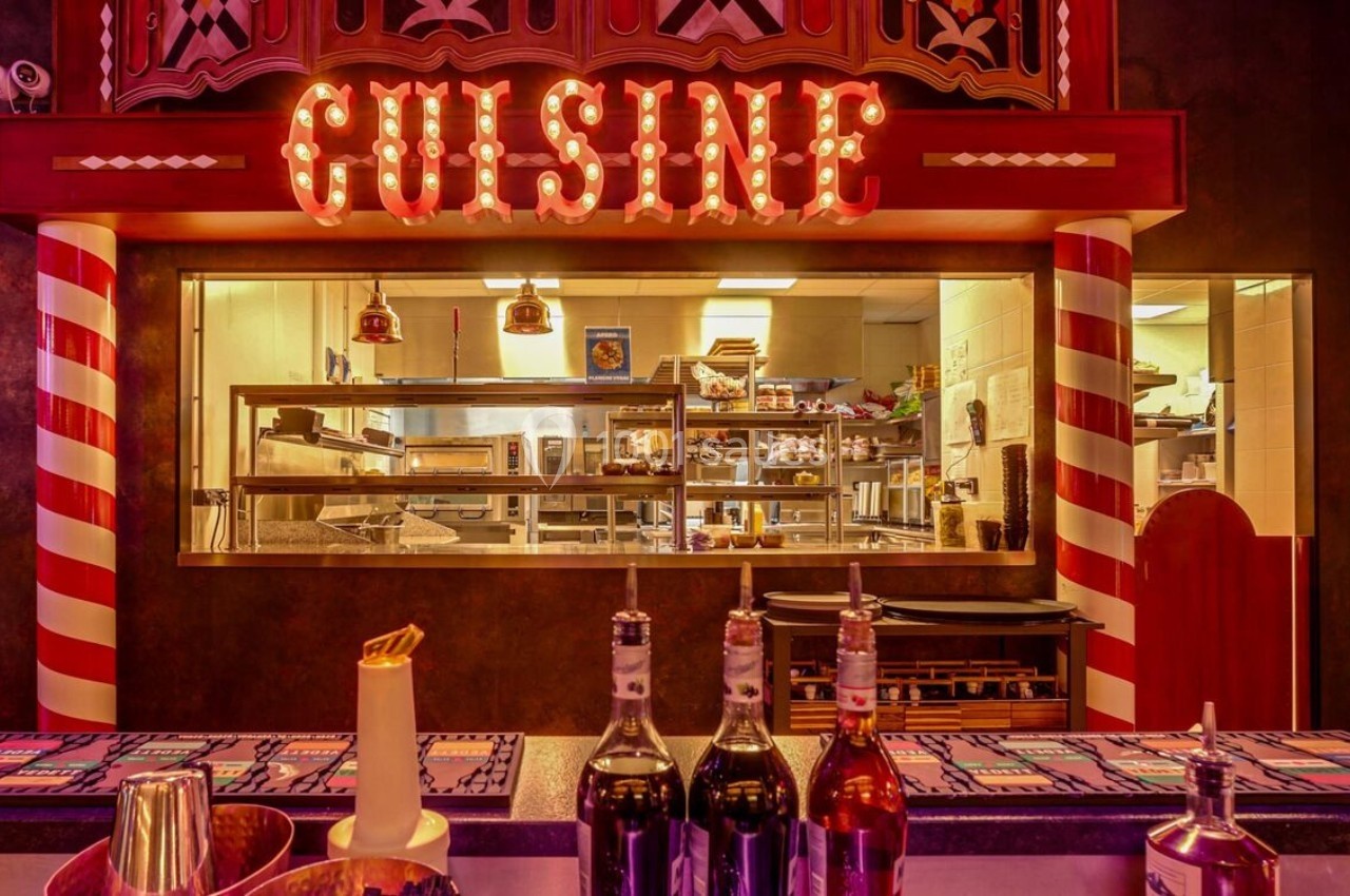 Vue d'une cuisine professionnelle éclairée, visible à travers une fenêtre sous une enseigne lumineuse ’CUISINE’.