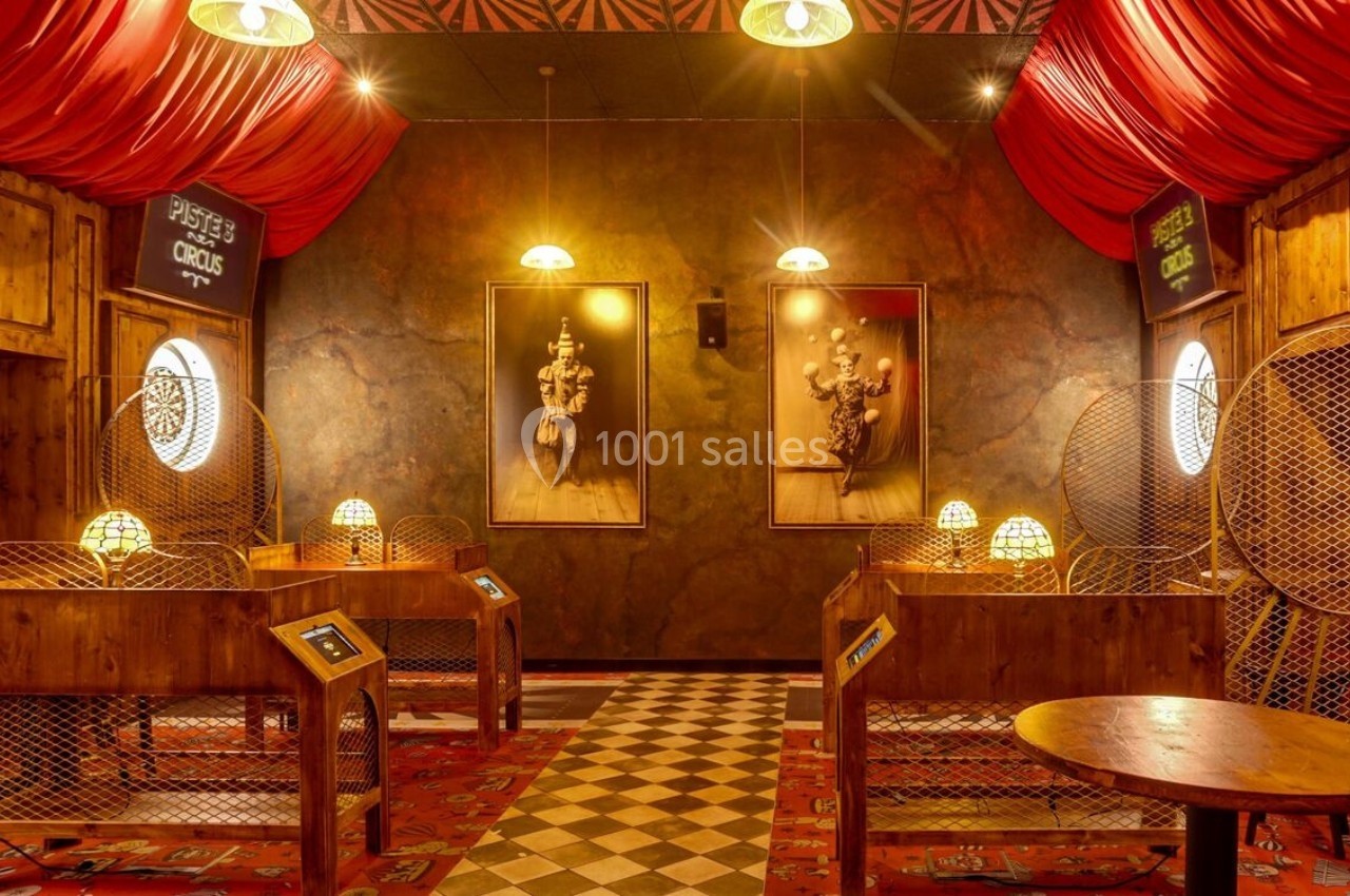 Salle décorée sur le thème du cirque avec des cabines en bois, des rideaux rouges et des portraits rétro éclairés.