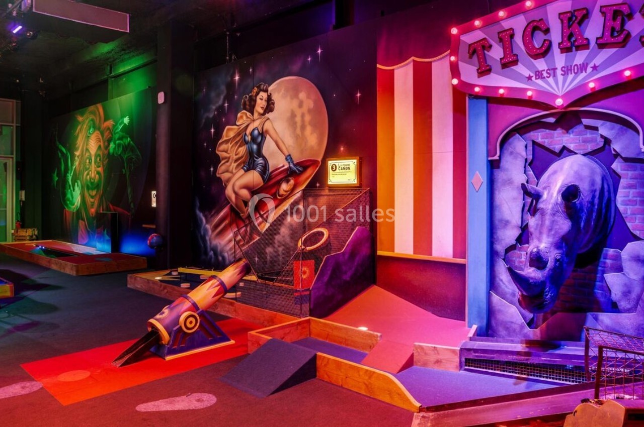 Décor coloré d'un mini-golf intérieur avec fresques rétro, fusée et éléments thématiques lumineux.