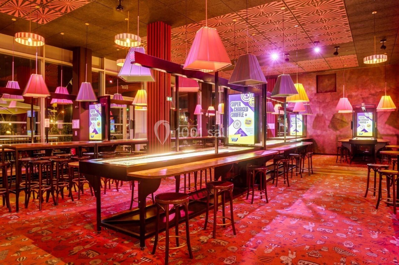 Salle de bar lumineuse avec un long comptoir central, des tabourets et des suspensions colorées au plafond.