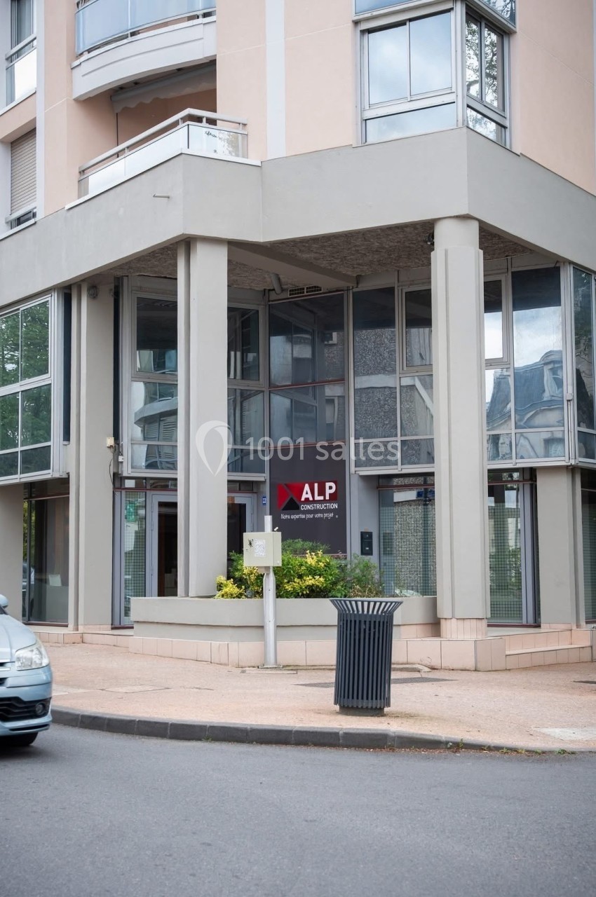 Façade d'un immeuble moderne avec une entrée vitrée et un panneau indiquant ’ALP’ près d'une rue passante.