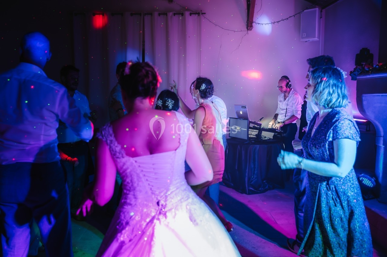 Des personnes dansent sous des lumières colorées près d'un DJ lors d'une fête ou d'un mariage.