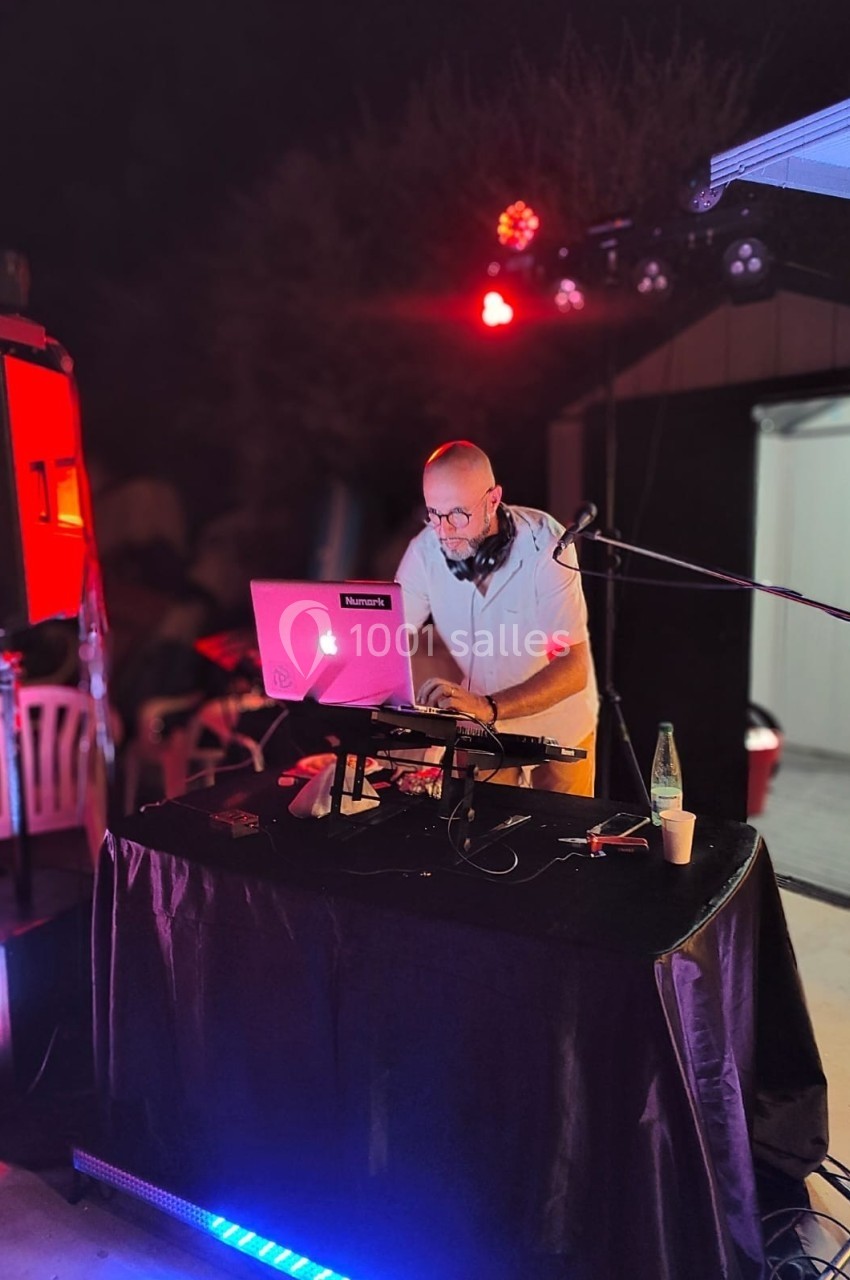Un DJ mixe de la musique sur une table équipée d'un ordinateur portable et de matériel audio lors d'un événement en soirée.