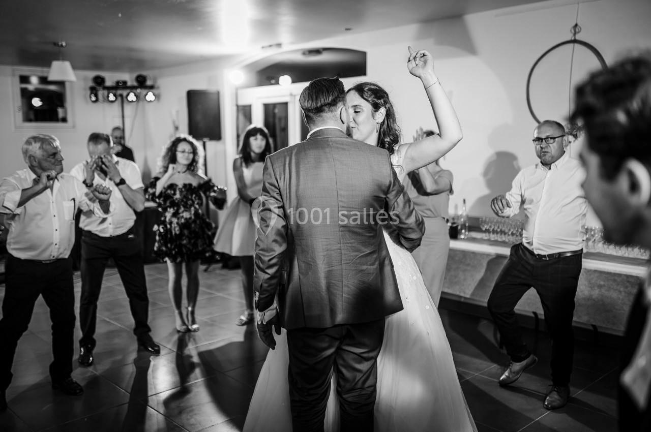 Un couple danse lors d'une réception, entouré d'invités applaudissant dans une salle éclairée.