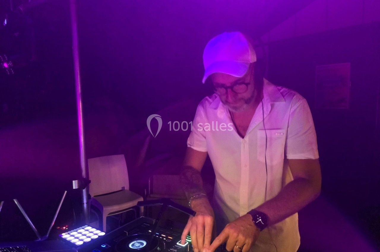 Un DJ portant une casquette blanche mixe de la musique sur une console dans une ambiance lumineuse violette.