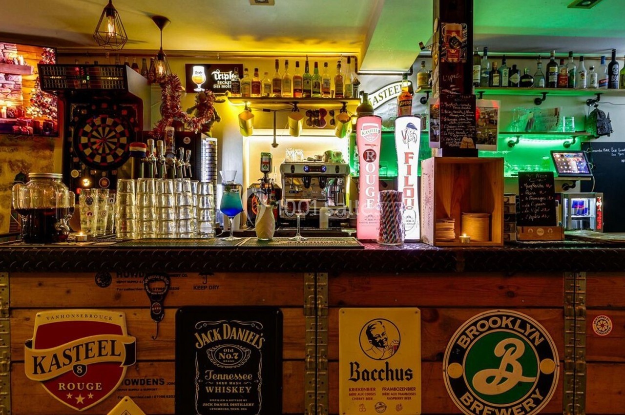 Bar avec comptoir en bois, décor lumineux, étagères de bouteilles, tireuses à bière et ambiance chaleureuse.