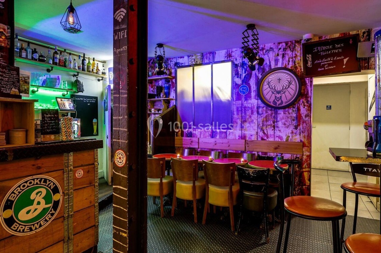 Intérieur d'un bar avec comptoir, tabourets, tables et chaises, éclairage coloré et décorations murales variées.