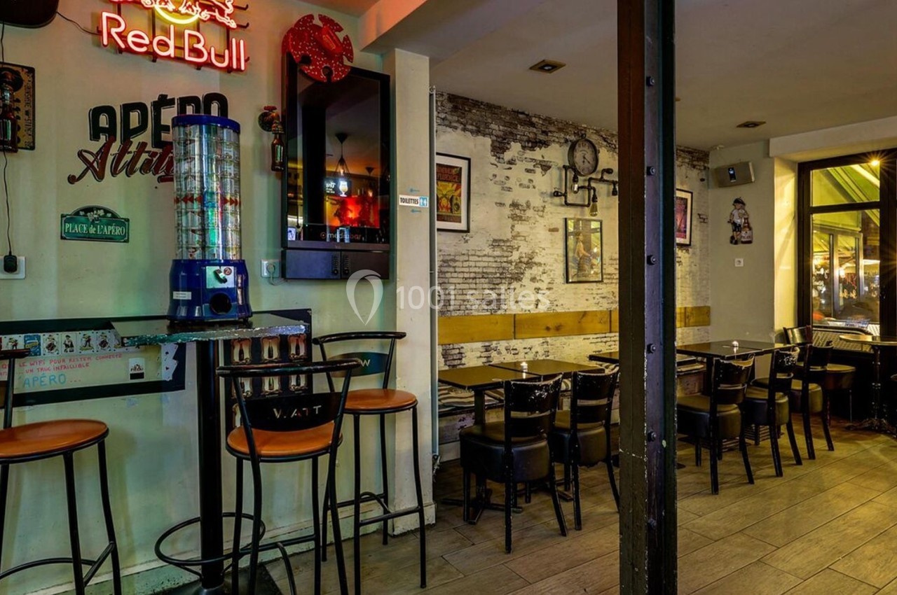 Intérieur d'un bar avec tables, chaises, murs décorés et enseigne lumineuse, ambiance chaleureuse et décontractée.