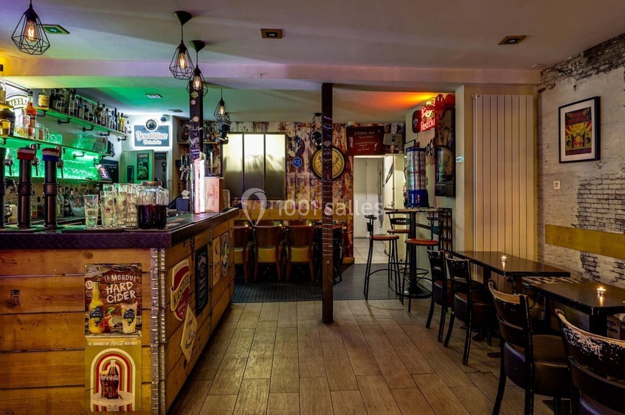 Intérieur d'un bar avec comptoir en bois, tables et chaises, éclairage coloré et décorations murales variées.