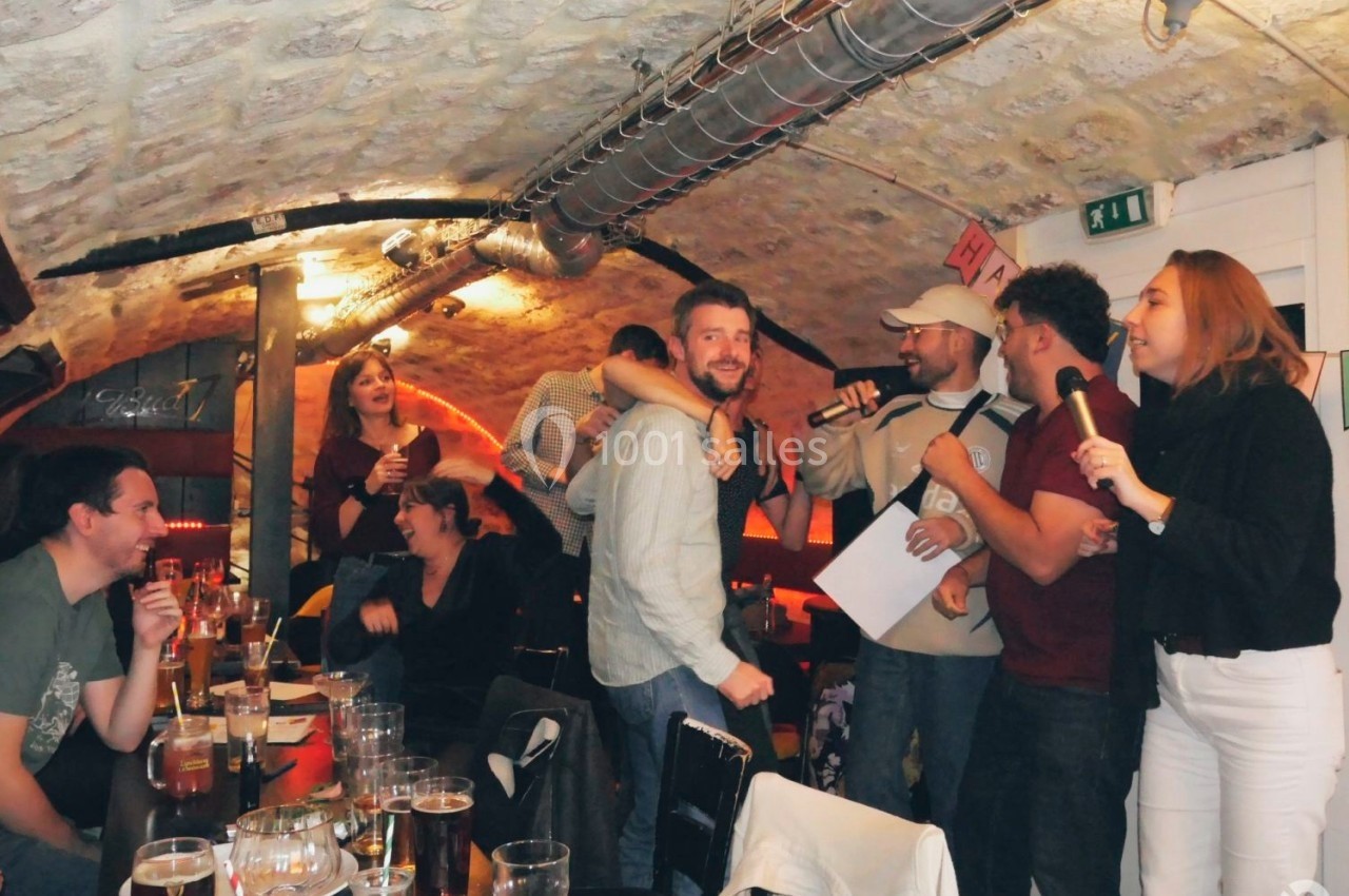 Groupe de personnes chantant et discutant dans un bar à l'ambiance chaleureuse avec des verres sur les tables.