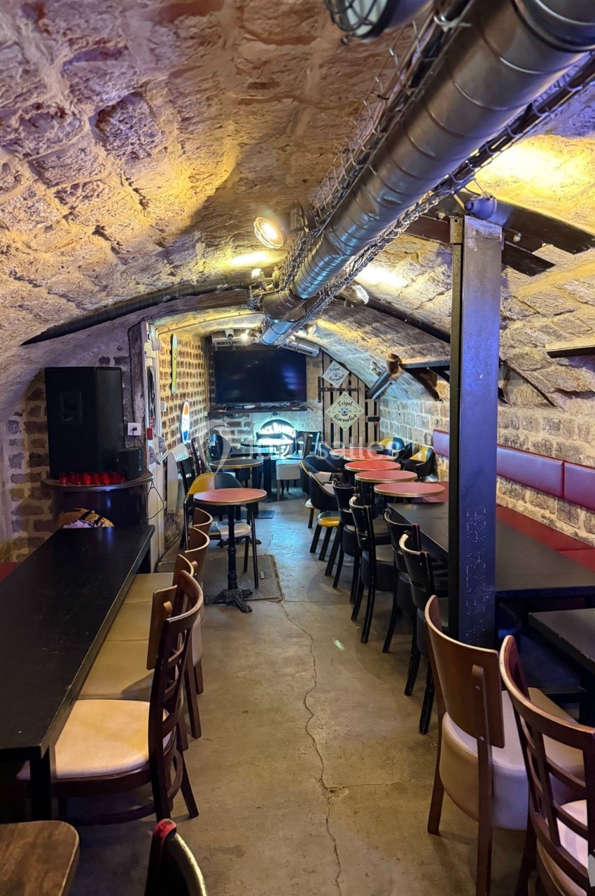 Salle voûtée en pierre avec tables et chaises disposées pour des repas ou réunions, éclairage chaleureux.