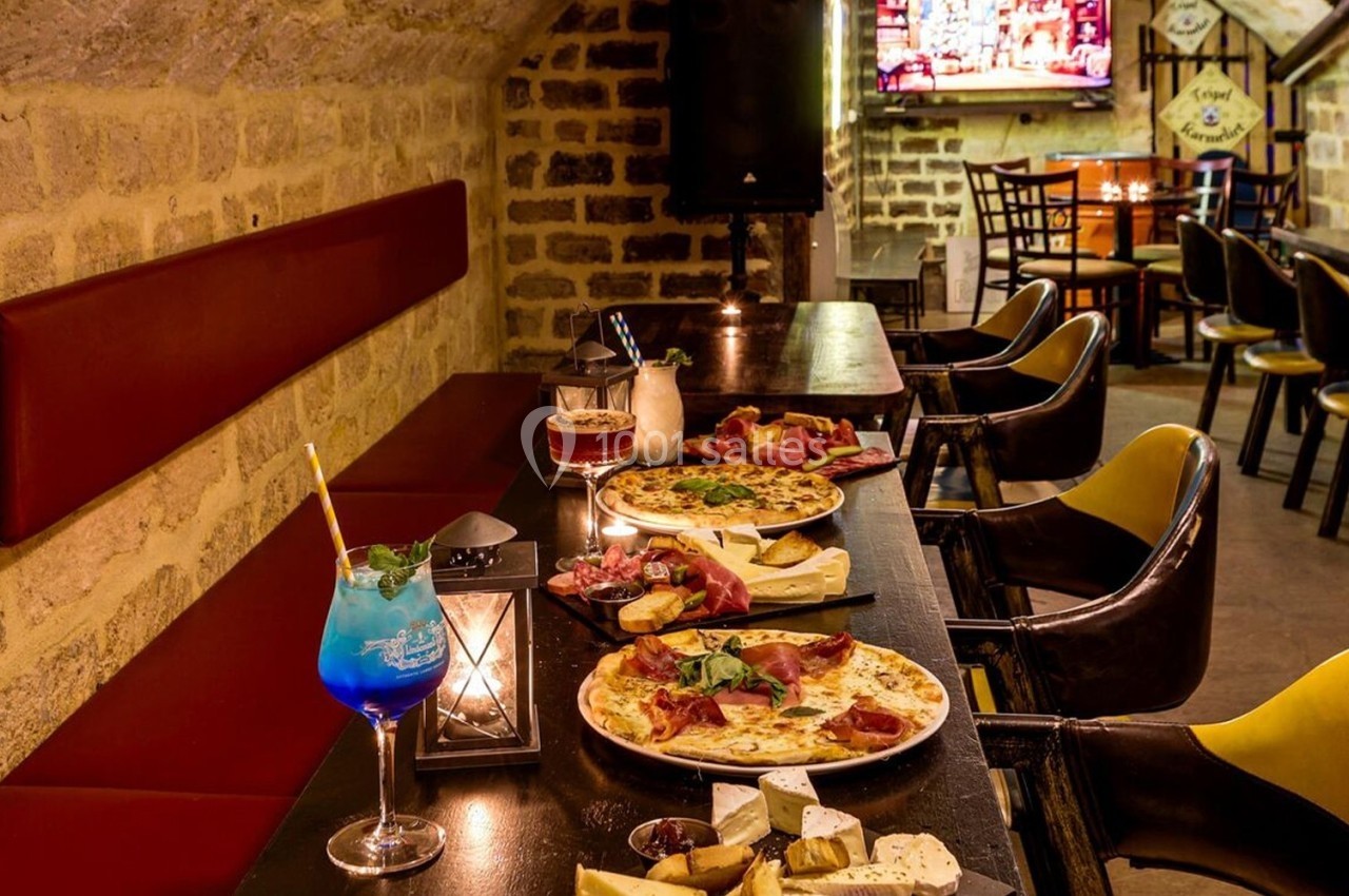 Salle de restaurant avec murs en pierre, tables garnies de pizzas, fromages et boissons colorées.