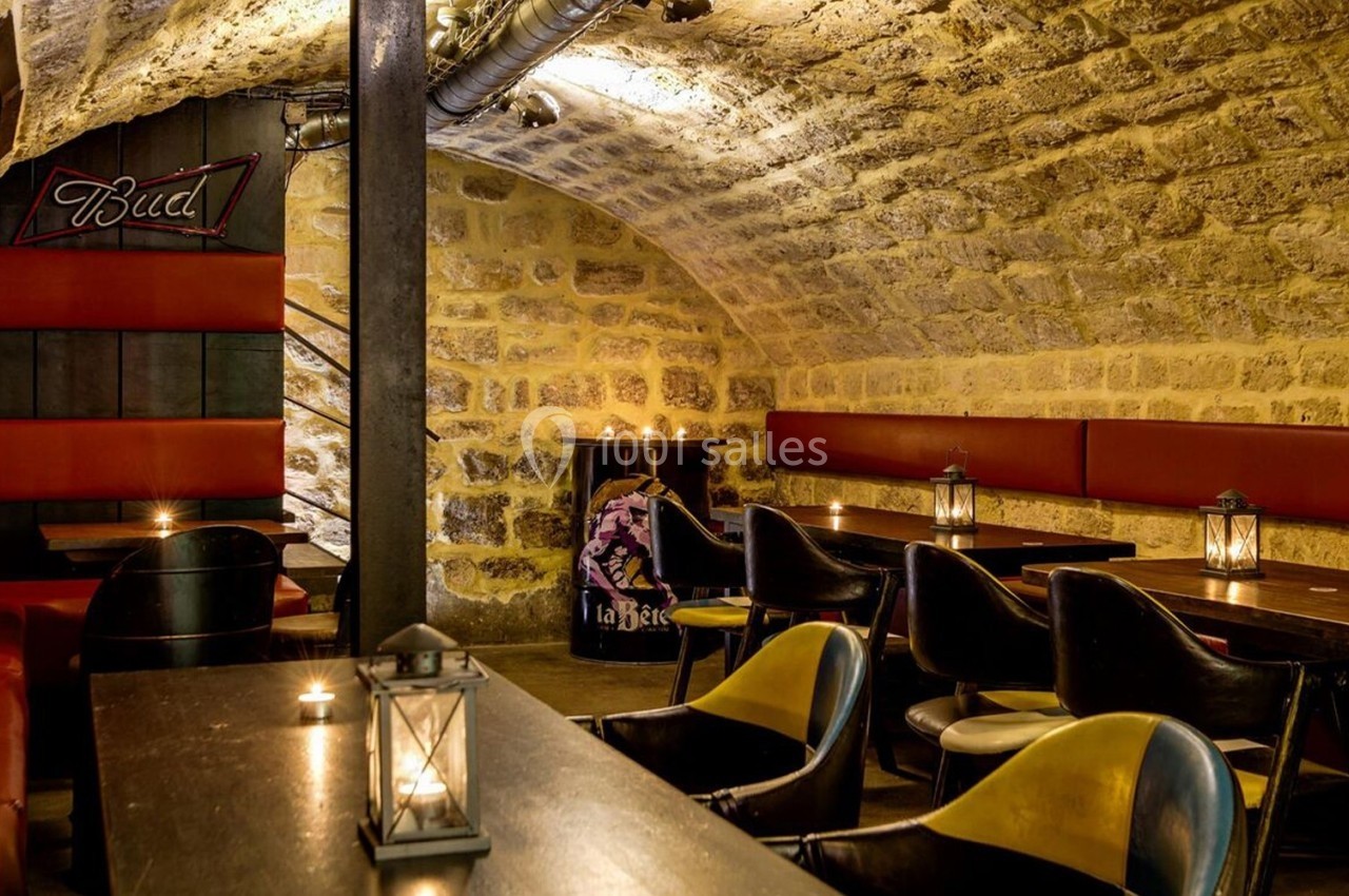 Salle voûtée en pierre avec banquettes rouges, tables en bois, chaises noires et éclairage tamisé par des lanternes.