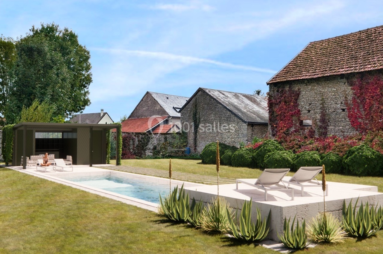 Piscine extérieure moderne avec terrasse, transats, pergola et jardin arboré entouré de bâtiments en pierre.