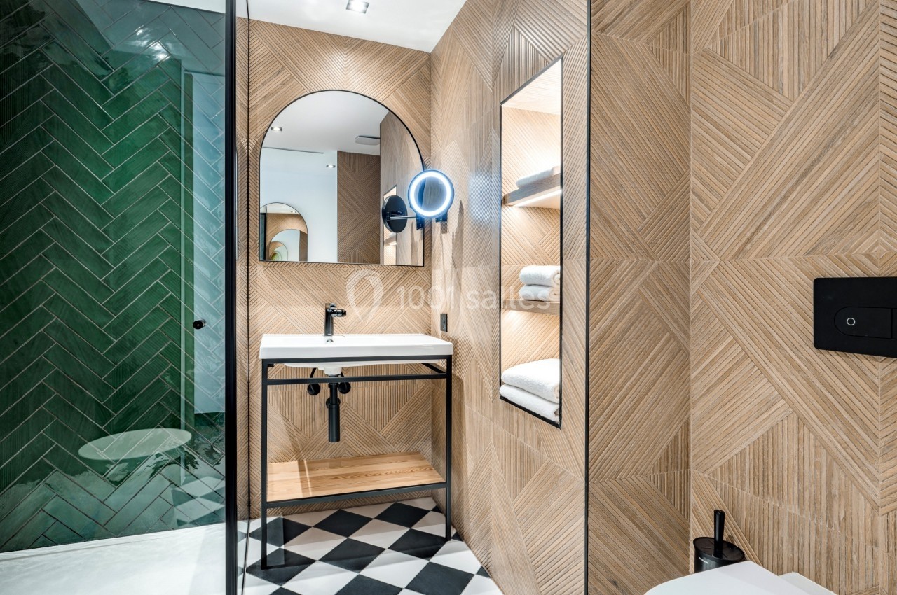 Salle de bain moderne avec carrelage géométrique, douche à paroi vitrée, miroir éclairé et lavabo minimaliste.