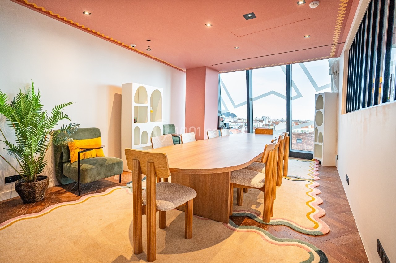 Salle de réunion lumineuse avec une grande table en bois, des chaises, un fauteuil vert et une plante décorative.