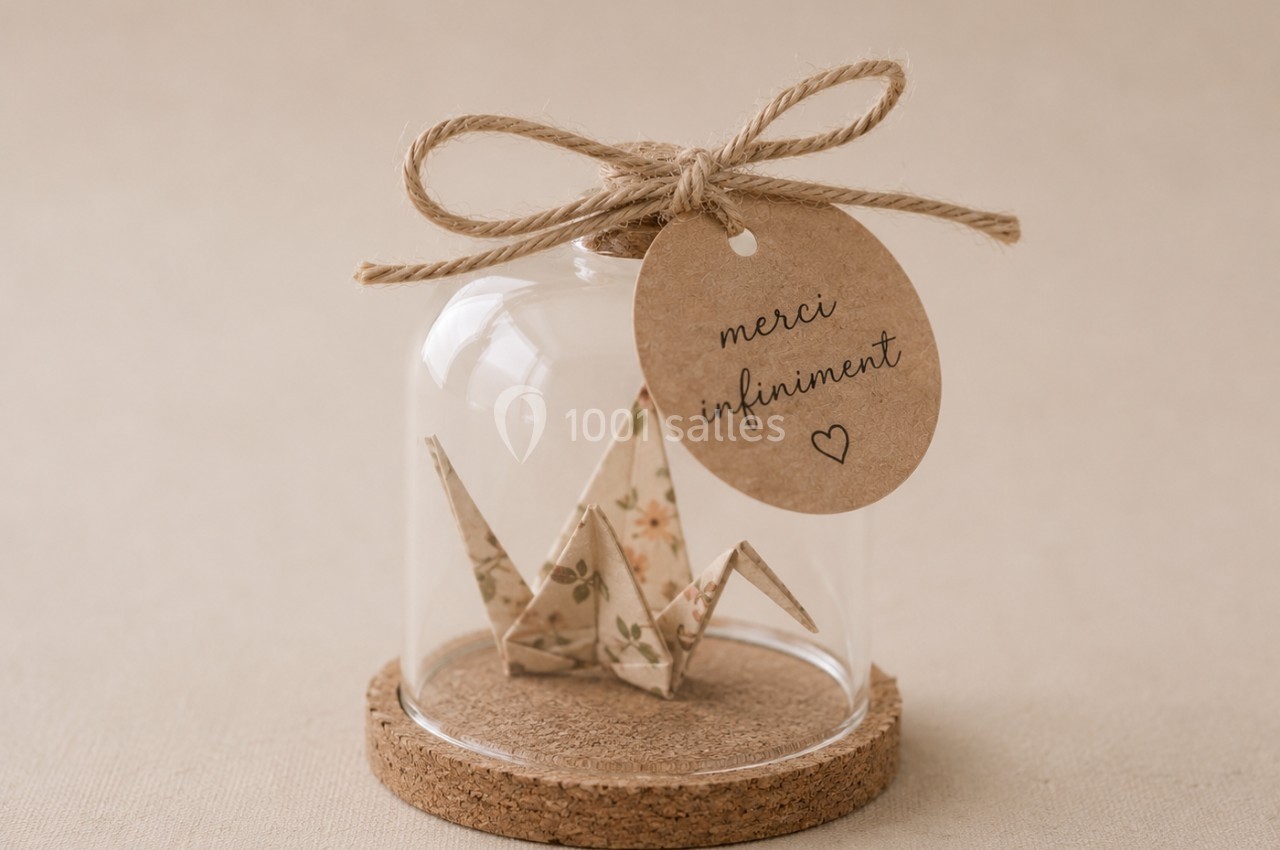 Origami de grue en papier fleuri sous une cloche en verre avec une étiquette en kraft portant l'inscription ’merci…