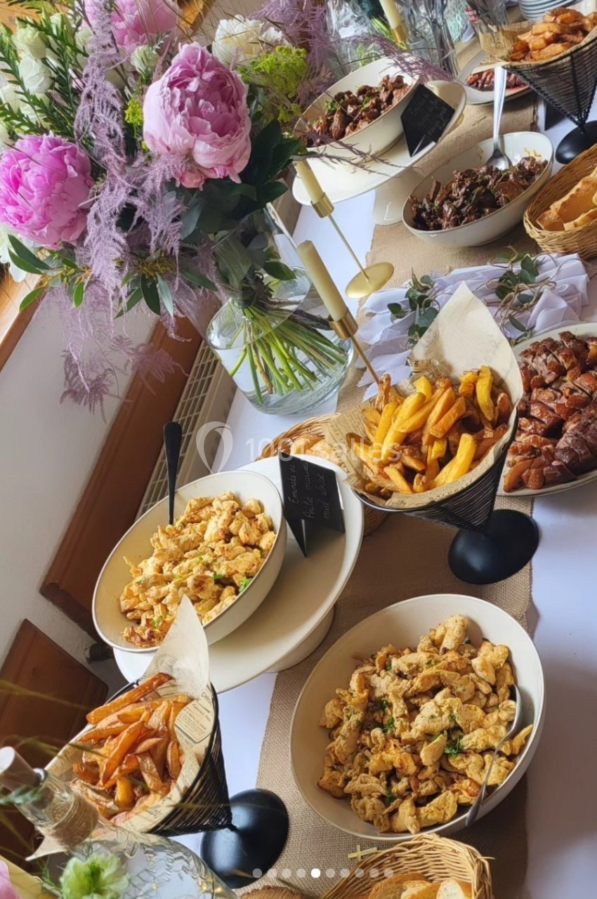 Buffet composé de plats variés, frites, salades et viandes, décoré de fleurs roses sur une table blanche.