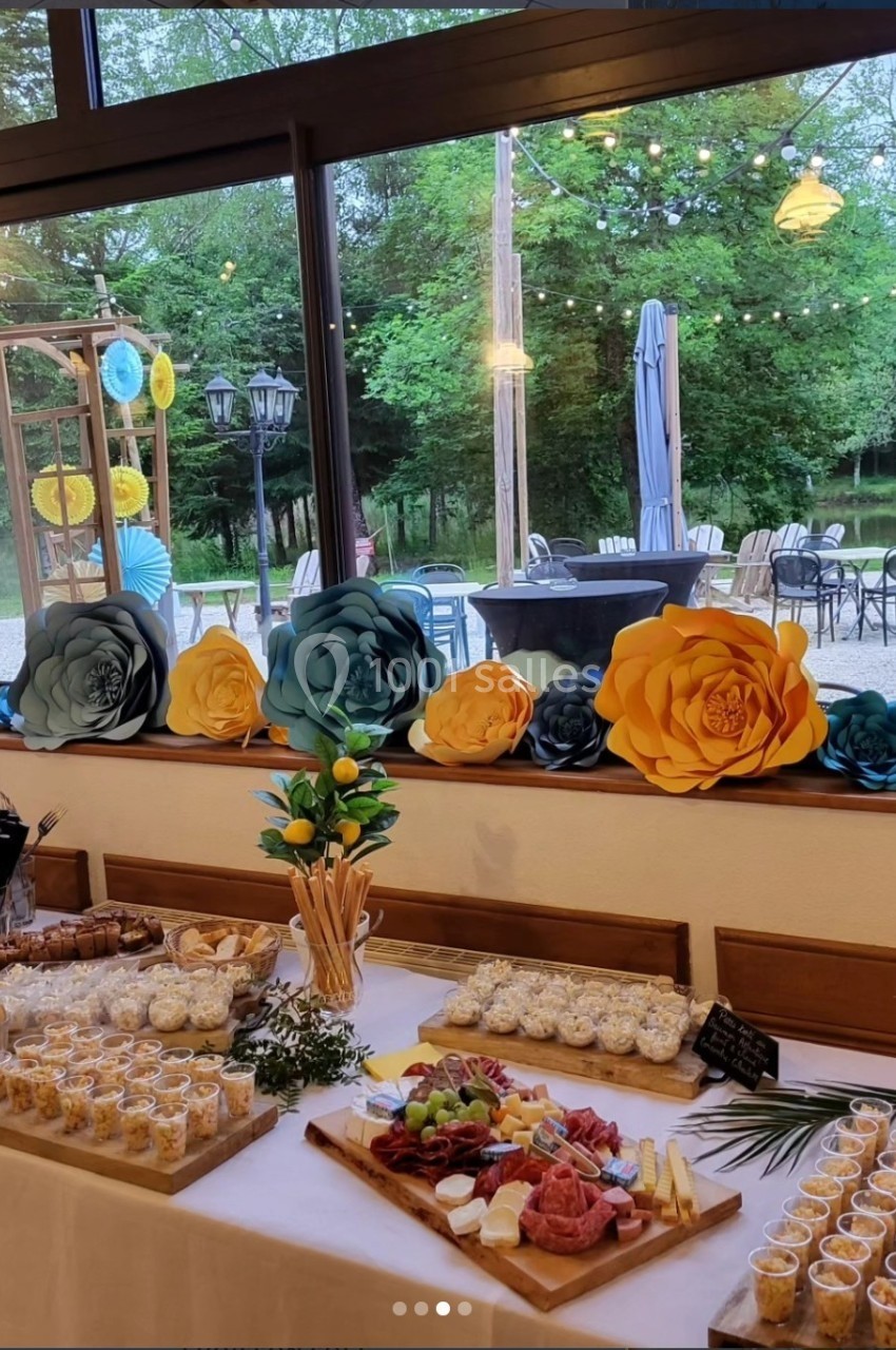 Table garnie de plats apéritifs variés devant une fenêtre décorée de fleurs en papier, vue sur un jardin extérieur.