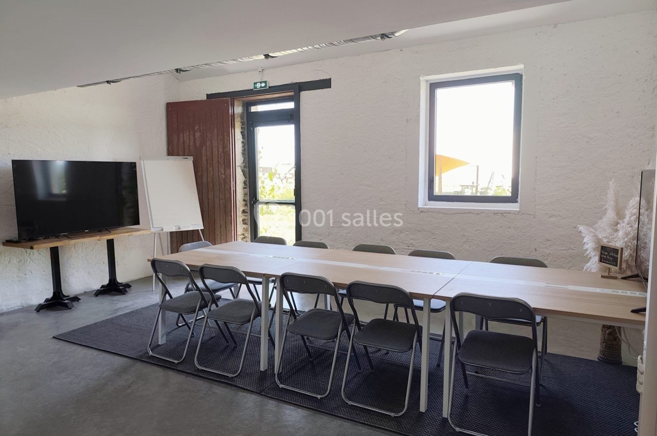 Salle de réunion lumineuse avec une grande table, des chaises, un tableau blanc et un écran près d'une fenêtre.