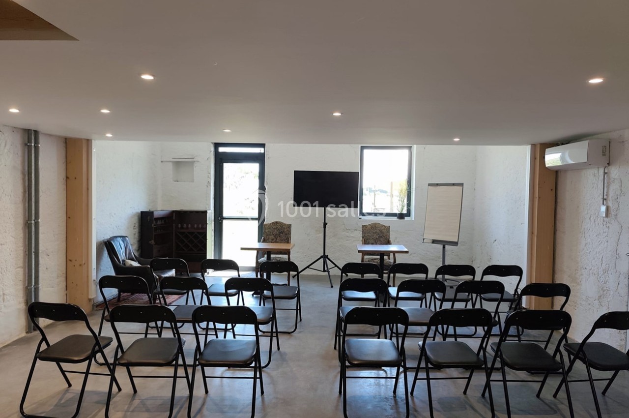 Salle de réunion équipée de chaises, tables, écran, tableau blanc et éclairage, prête pour une présentation.