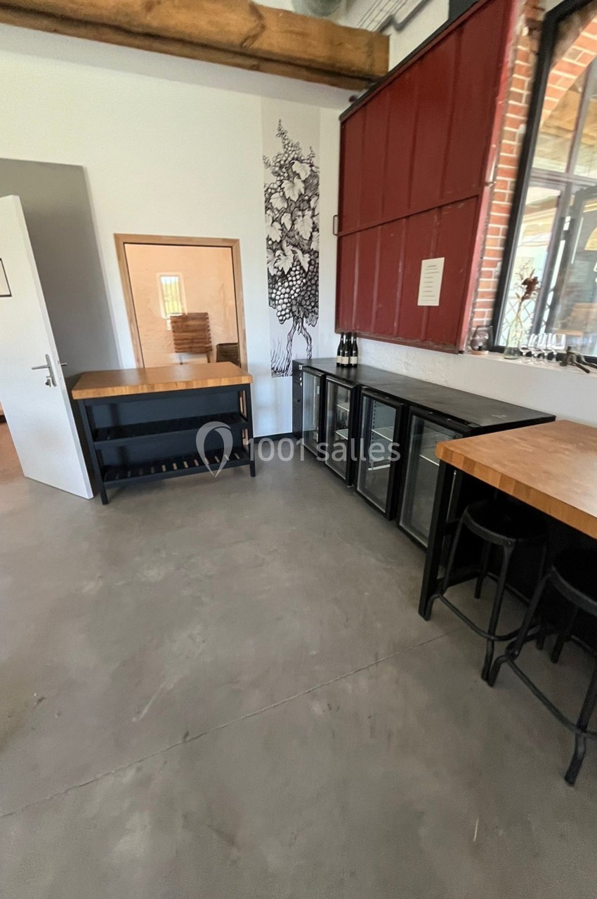 Espace intérieur avec comptoirs en bois, réfrigérateurs vitrés, tabourets et décoration murale végétale.