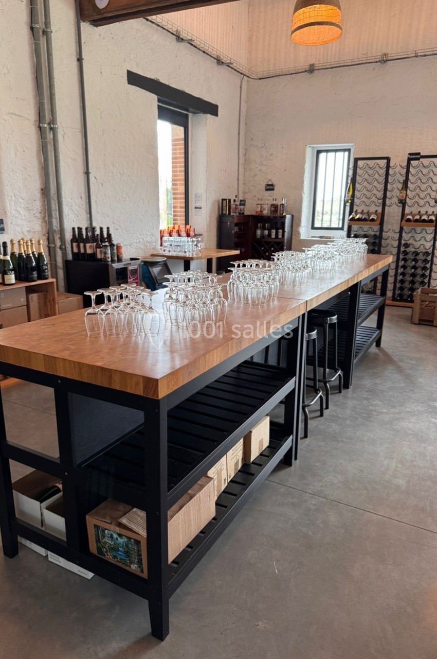Salle de dégustation avec un long comptoir en bois, verres alignés, bouteilles et casiers à vin en arrière-plan.