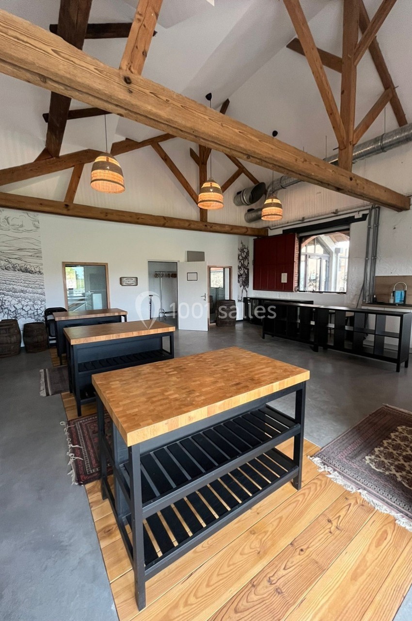 Salle lumineuse avec poutres apparentes, tables en bois et étagères noires, décor rustique et moderne.