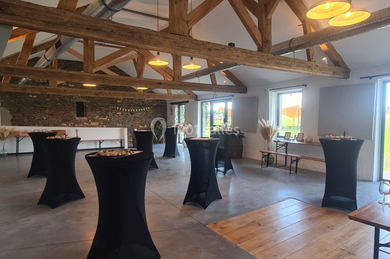 Salle lumineuse avec poutres apparentes, tables hautes drapées de noir et décorations minimalistes.