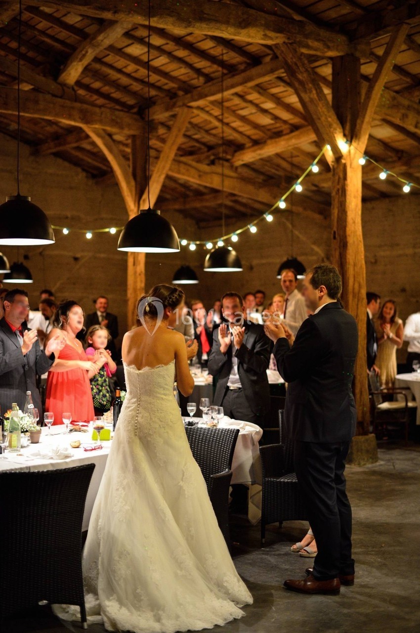 Des invités applaudissent un couple lors d'une réception de mariage dans une salle avec des poutres apparentes et des…