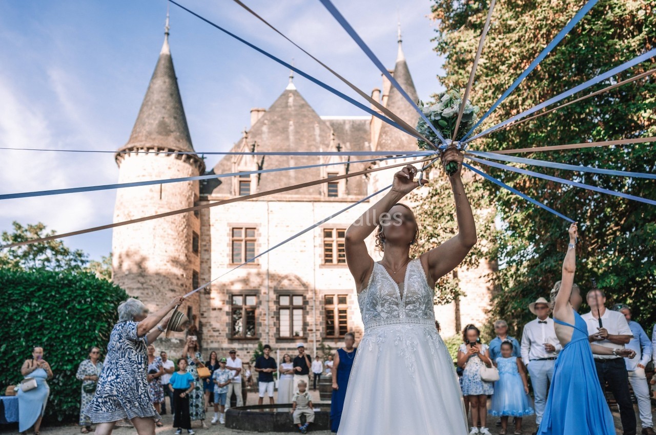 Une mariée danse en tenant des rubans colorés devant un château, entourée d'invités lors d'une célébration.