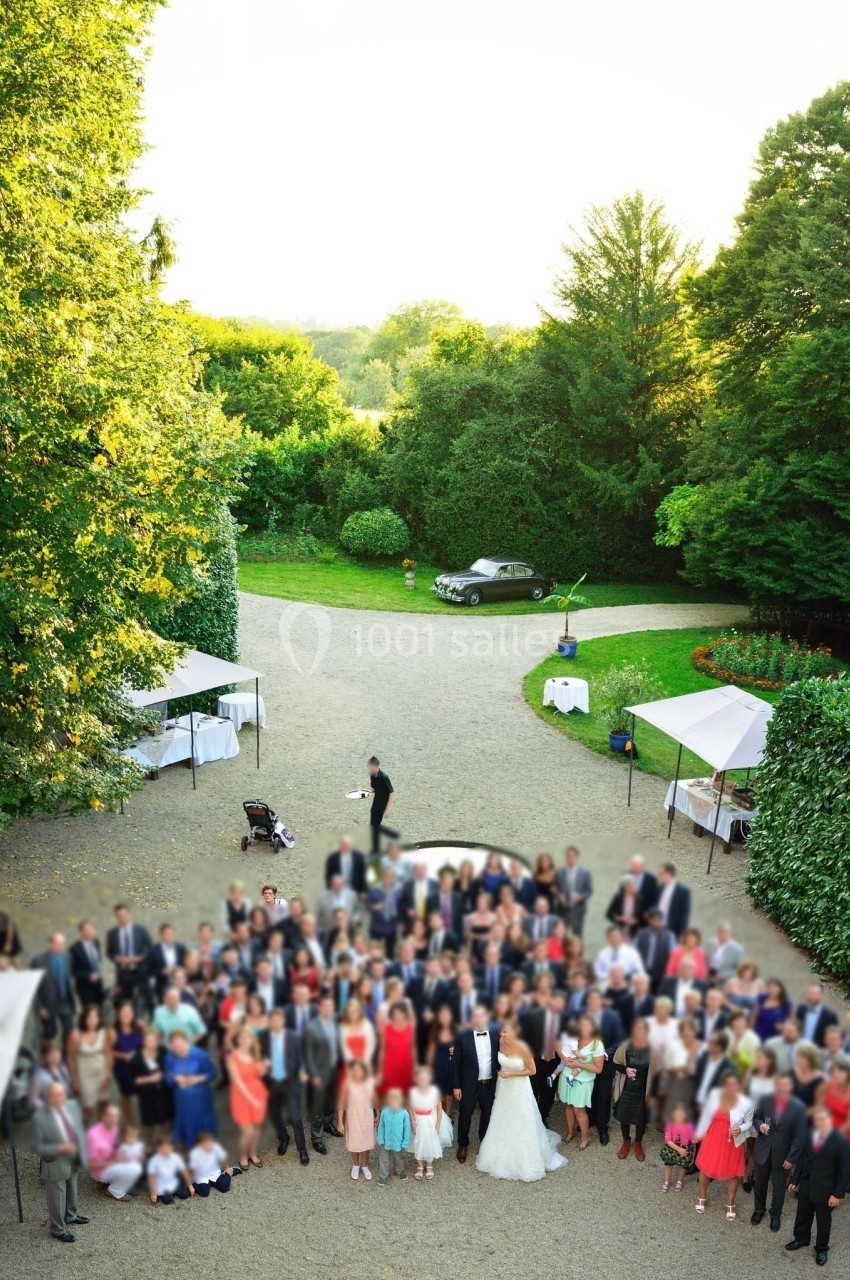 Groupe de personnes rassemblées en extérieur pour une photo de mariage, entourées de verdure et de tentes blanches.