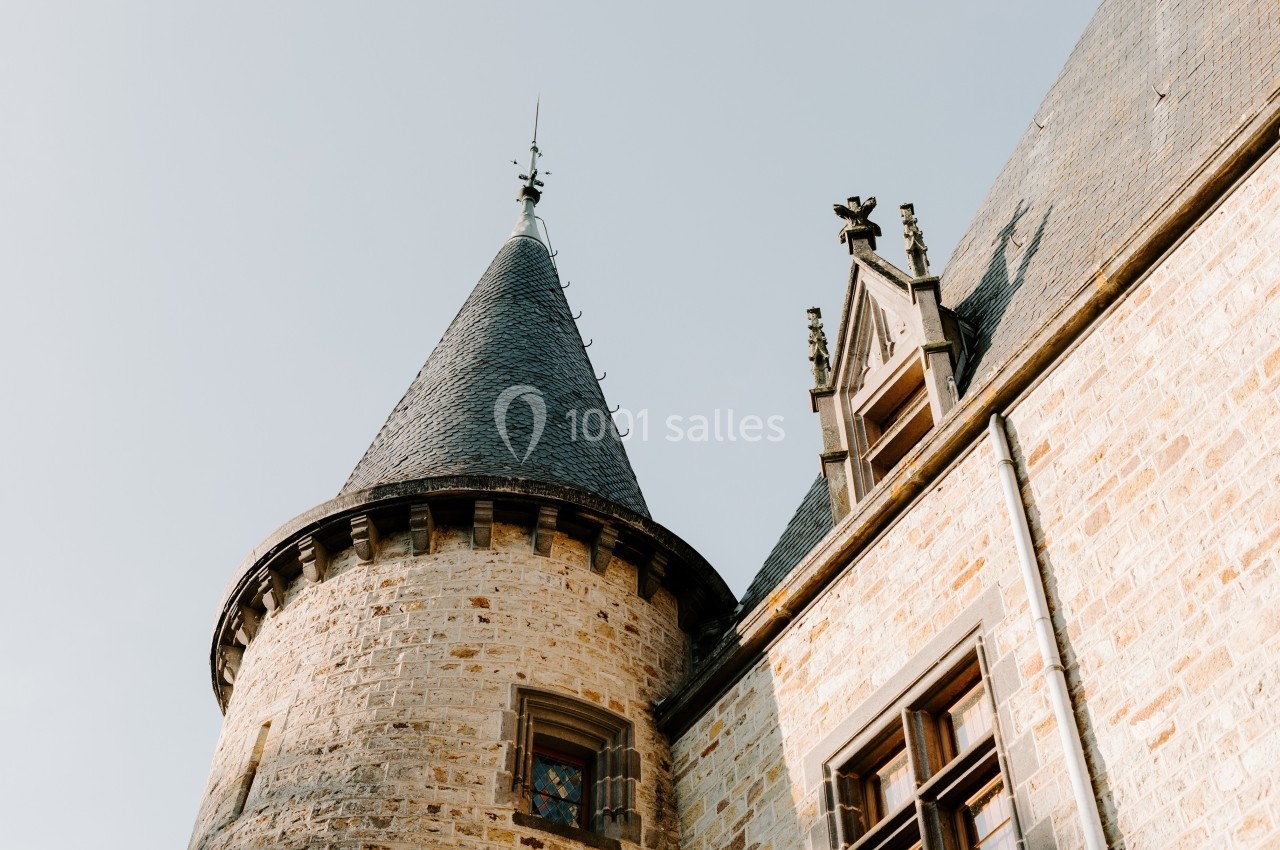 Tour en pierre avec toit conique et fenêtres, partie d'un bâtiment historique sous un ciel clair.