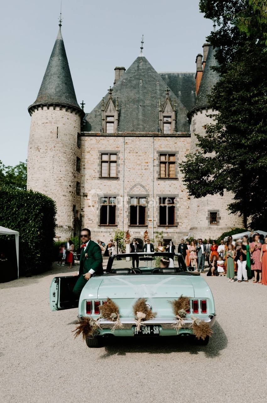 Voiture décapotable verte décorée de fleurs devant un château, avec des invités en arrière-plan.