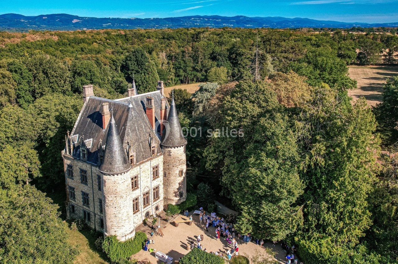 Vue aérienne d'un château entouré de verdure avec des visiteurs rassemblés dans la cour par une journée ensoleillée.