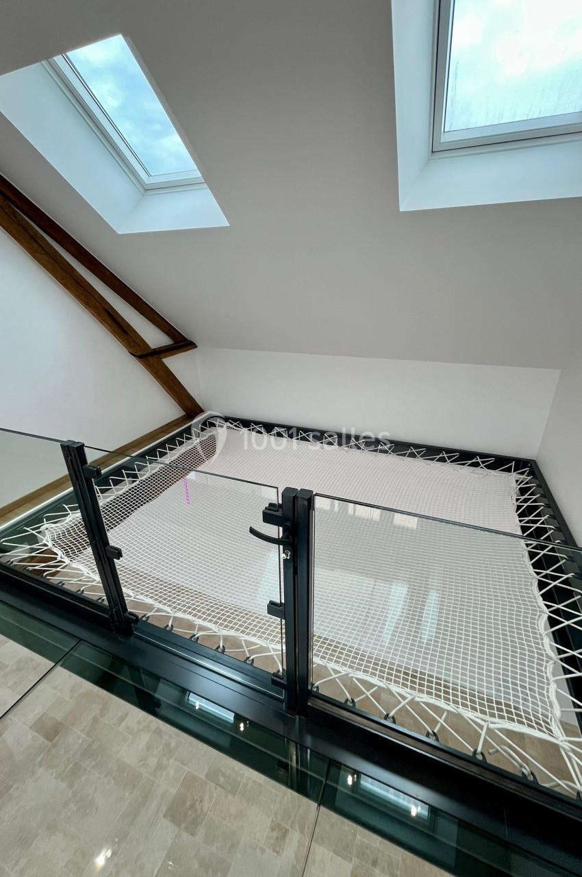 Filet suspendu installé dans un espace mezzanine lumineux avec garde-corps en verre et fenêtres de toit.