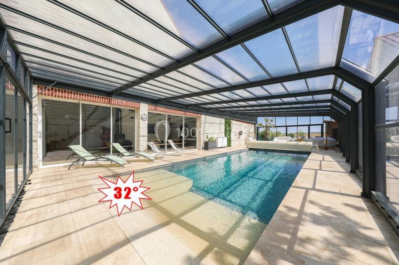 Piscine intérieure avec toit transparent, entourée de chaises longues, affichant une température de 32 degrés.