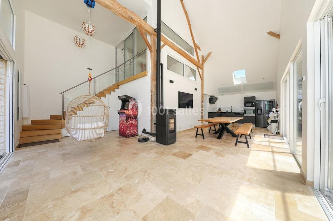 Intérieur lumineux avec mezzanine, escalier en bois, poêle à bois, table en bois massif et cuisine ouverte moderne.