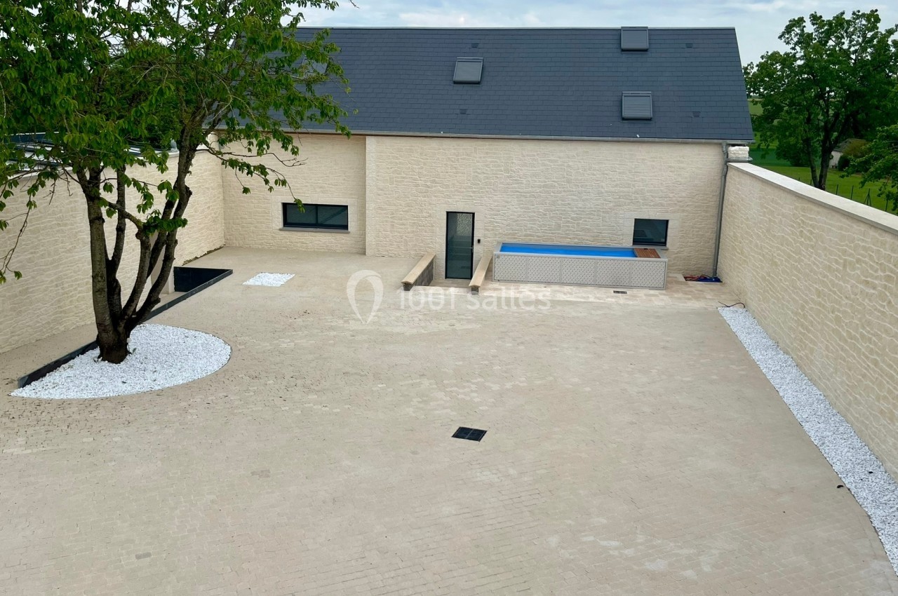 Cour pavée avec un arbre, des zones de gravier blanc, une piscine et une maison moderne en arrière-plan.