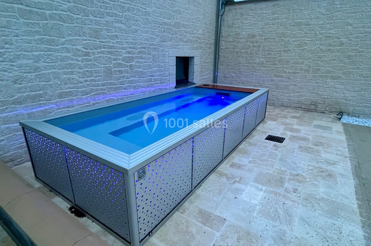 Piscine hors-sol rectangulaire en métal perforé, installée sur une terrasse en pierre, éclairée par des lumières bleues.