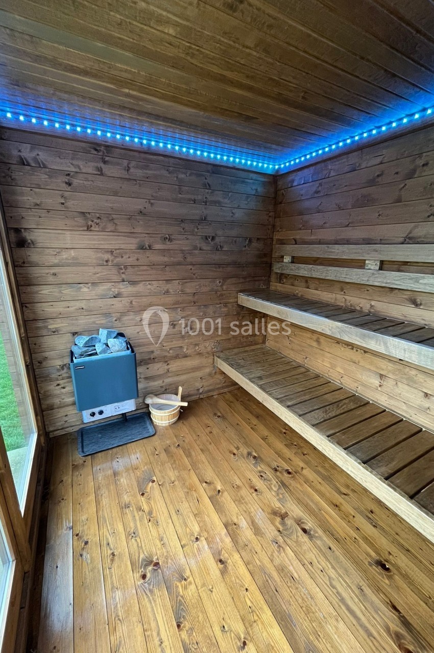 Intérieur d'un sauna en bois avec bancs, poêle à pierres et éclairage LED bleu au plafond.