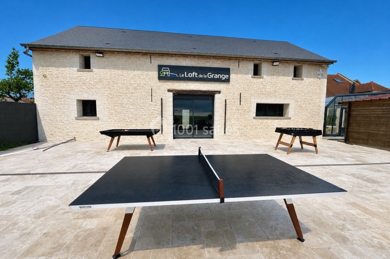 Table de ping-pong en extérieur devant un bâtiment en pierre avec une enseigne ’Le Loft de la Grange’.