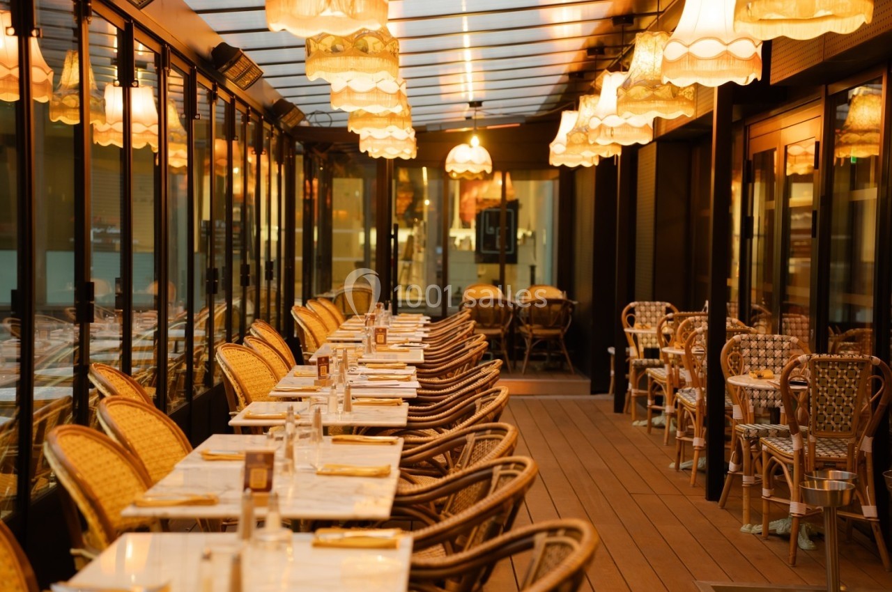 Terrasse couverte d'un restaurant avec tables dressées, chaises en osier et éclairage chaleureux de suspensions.