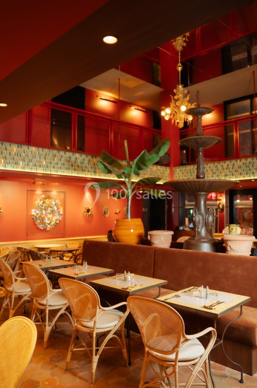 Salle de restaurant aux tons chauds avec tables en bois, chaises en rotin, plantes et décoration murale colorée.